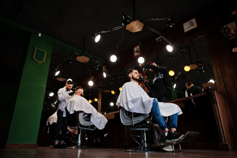 wo men sitting in the chairs and hairdressers making haircut for them, spot lights above them