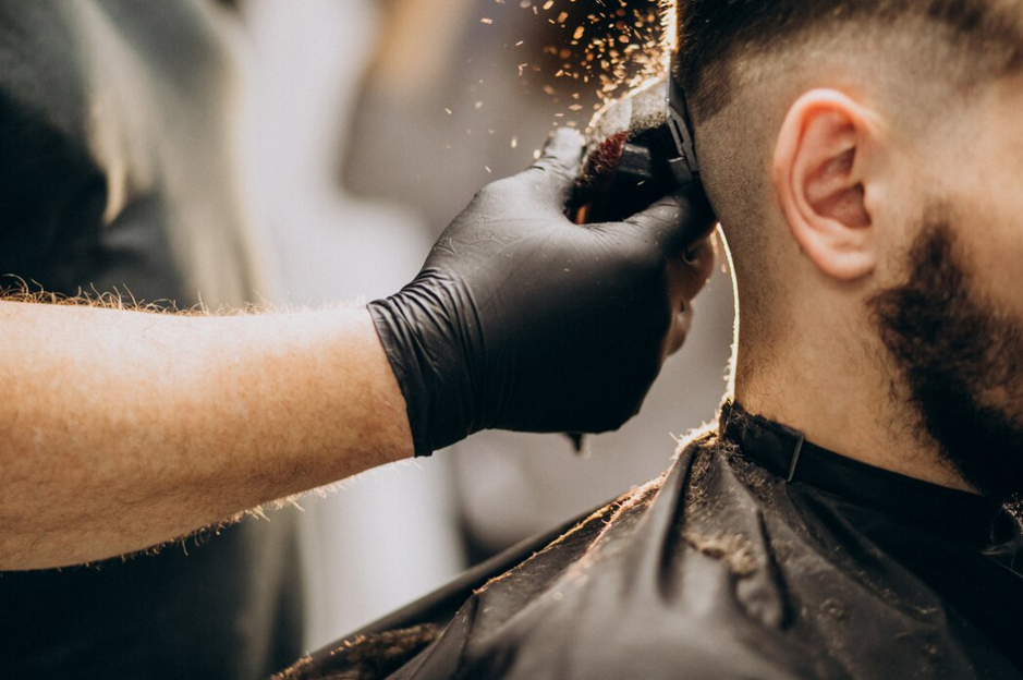 A barber's gloved hand trims the back of a client's head