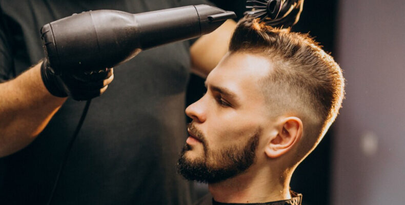 A barber in black gloves uses a hair dryer on a client's freshly cut high fade hairstyle