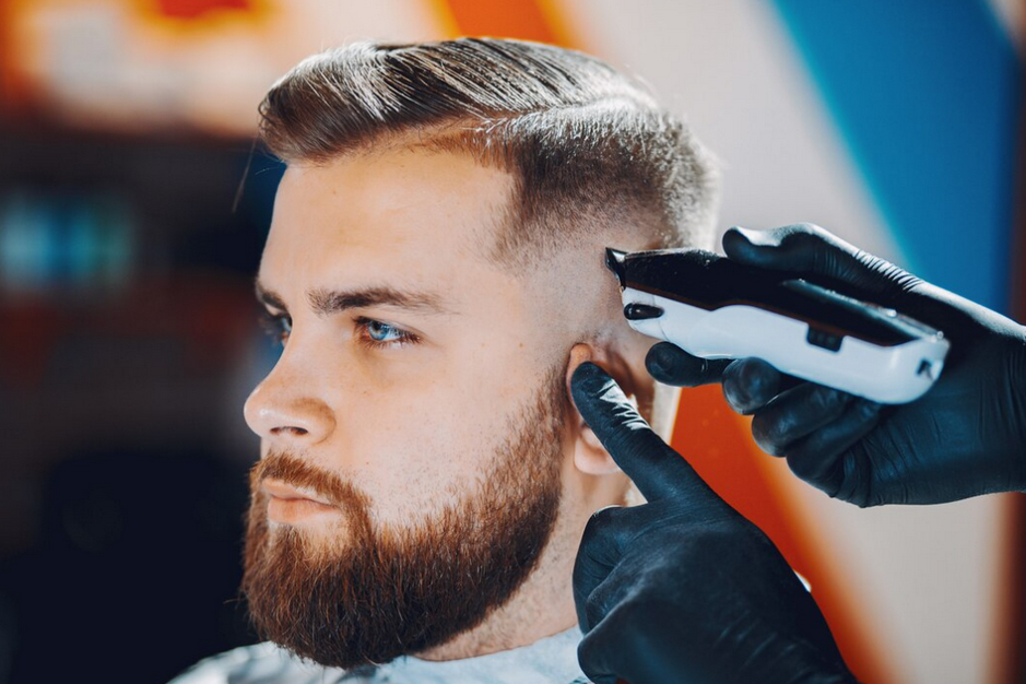 man getting his sideburns trimmed with an electric clipper by a gloved barber.