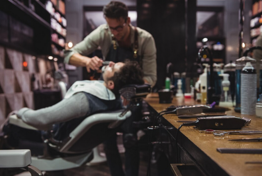 Barber trimming customer's beard in a modern shop with tools on the counter