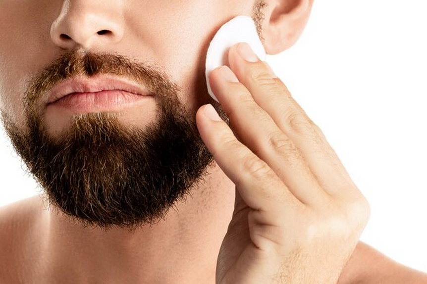 Bearded man using cotton pads on his face.