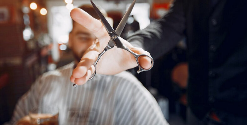 Hand holding scissors in front of a blurred barber shop background.