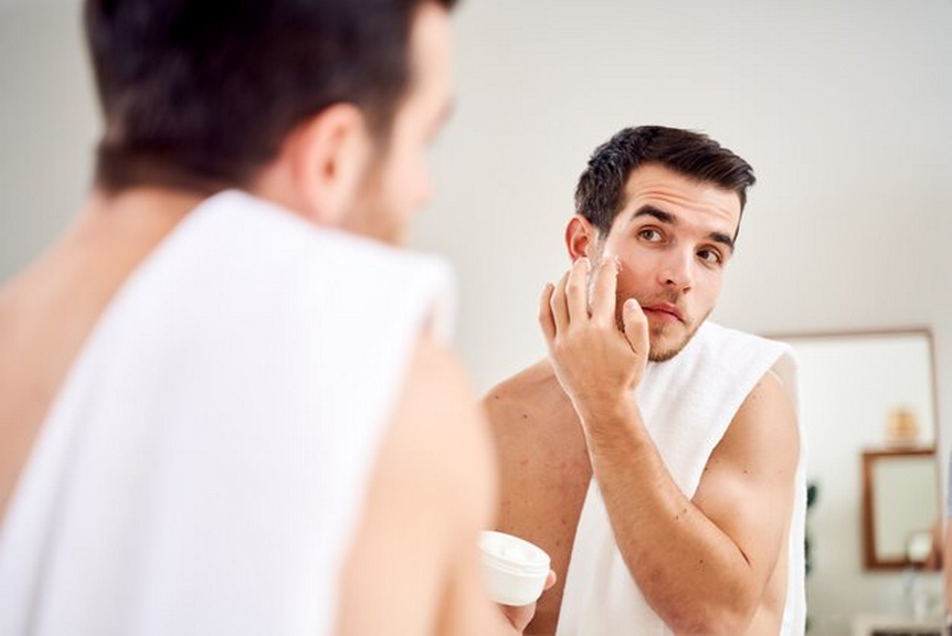 Man performing skincare routine in front of a mirror